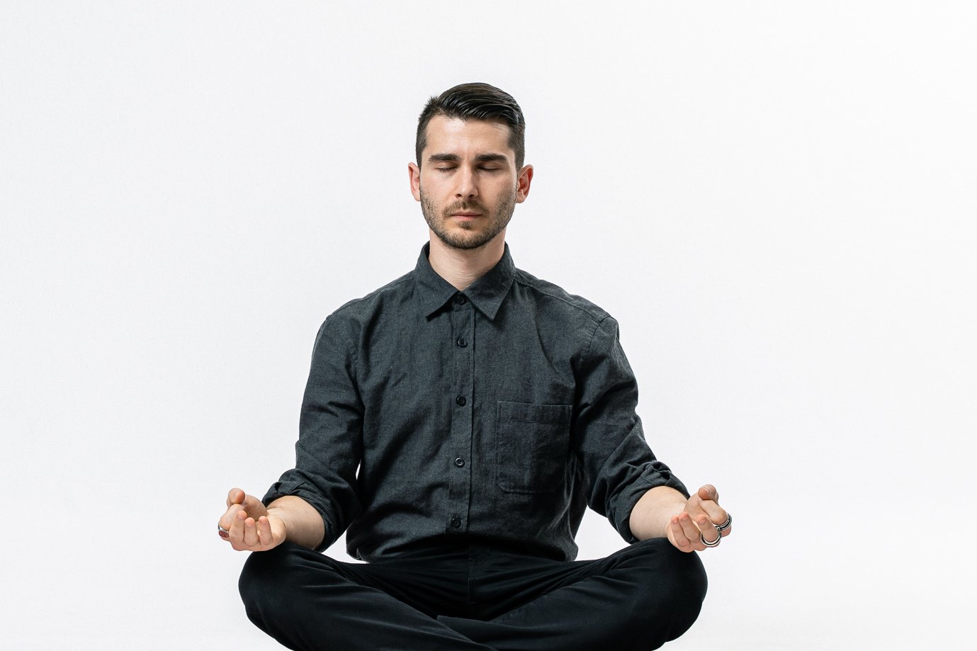 Vincenzo Rocco sitzt im Schneidersitz auf dem Boden, mit geschlossenen Augen und leicht geöffneten Händen auf den Knien, und meditiert vor einem weißen Hintergrund