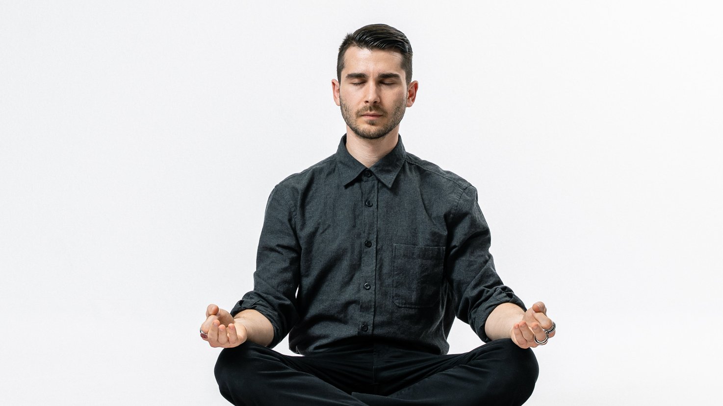 Vincenzo Rocco sitzt im Schneidersitz auf dem Boden, mit geschlossenen Augen und leicht geöffneten Händen auf den Knien, und meditiert vor einem weißen Hintergrund