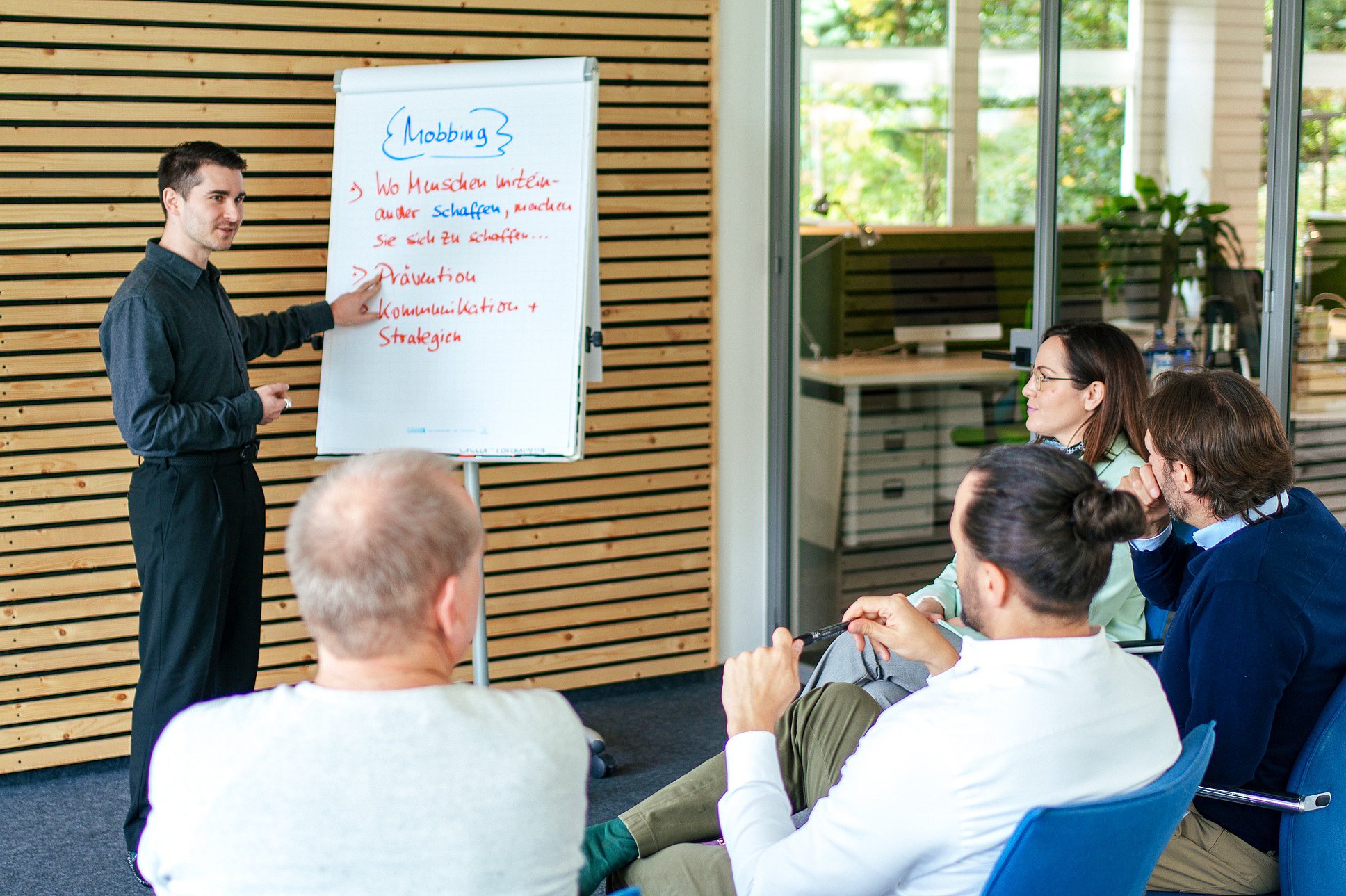 Vincenzo Rocco steht vor einer kleinen Gruppe sitzender Personen und präsentiert Inhalte zum Thema Mobbing auf einem Flipchart