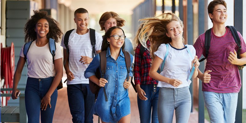 Eine Gruppe fröhlicher Jugendlicher läuft gemeinsam Richtung Schule.