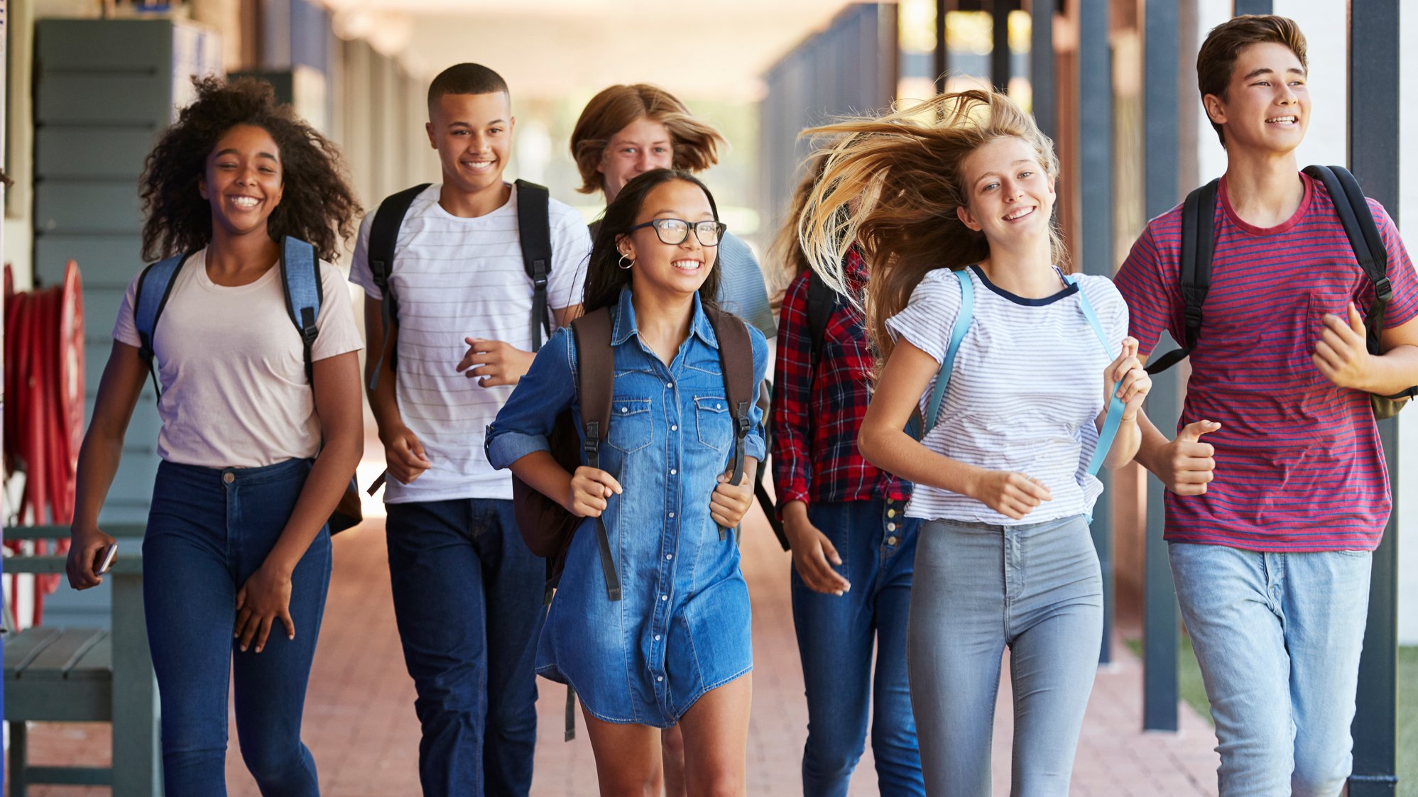 Eine Gruppe fröhlicher Jugendlicher läuft gemeinsam Richtung Schule.