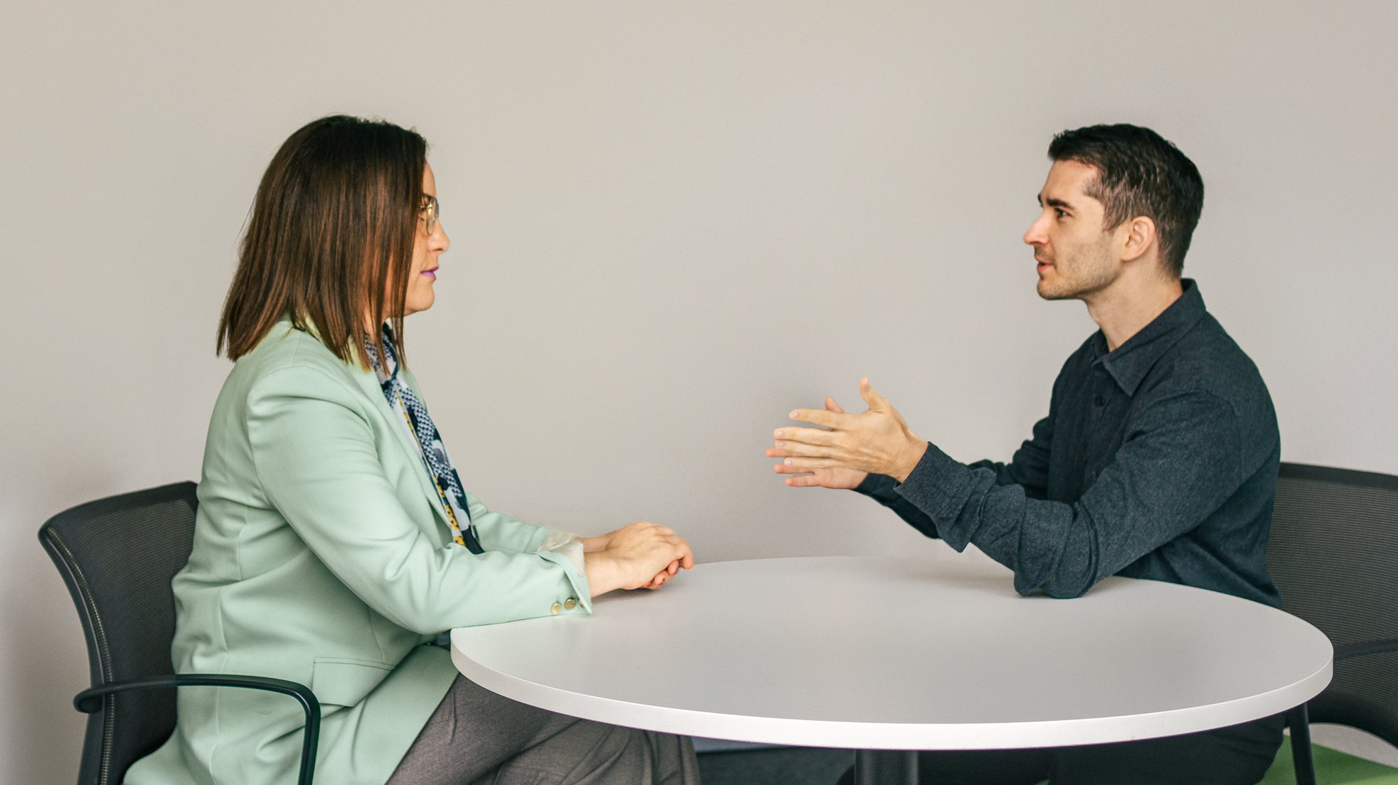 Eine Frau und Vincenzo Rocco sitzen sich an einem runden Tisch gegenüber und führen ein konzentriertes coaching Gespräch
